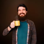 Homem sorridente com barba bebe uma xícara amarela de café Café Pelé